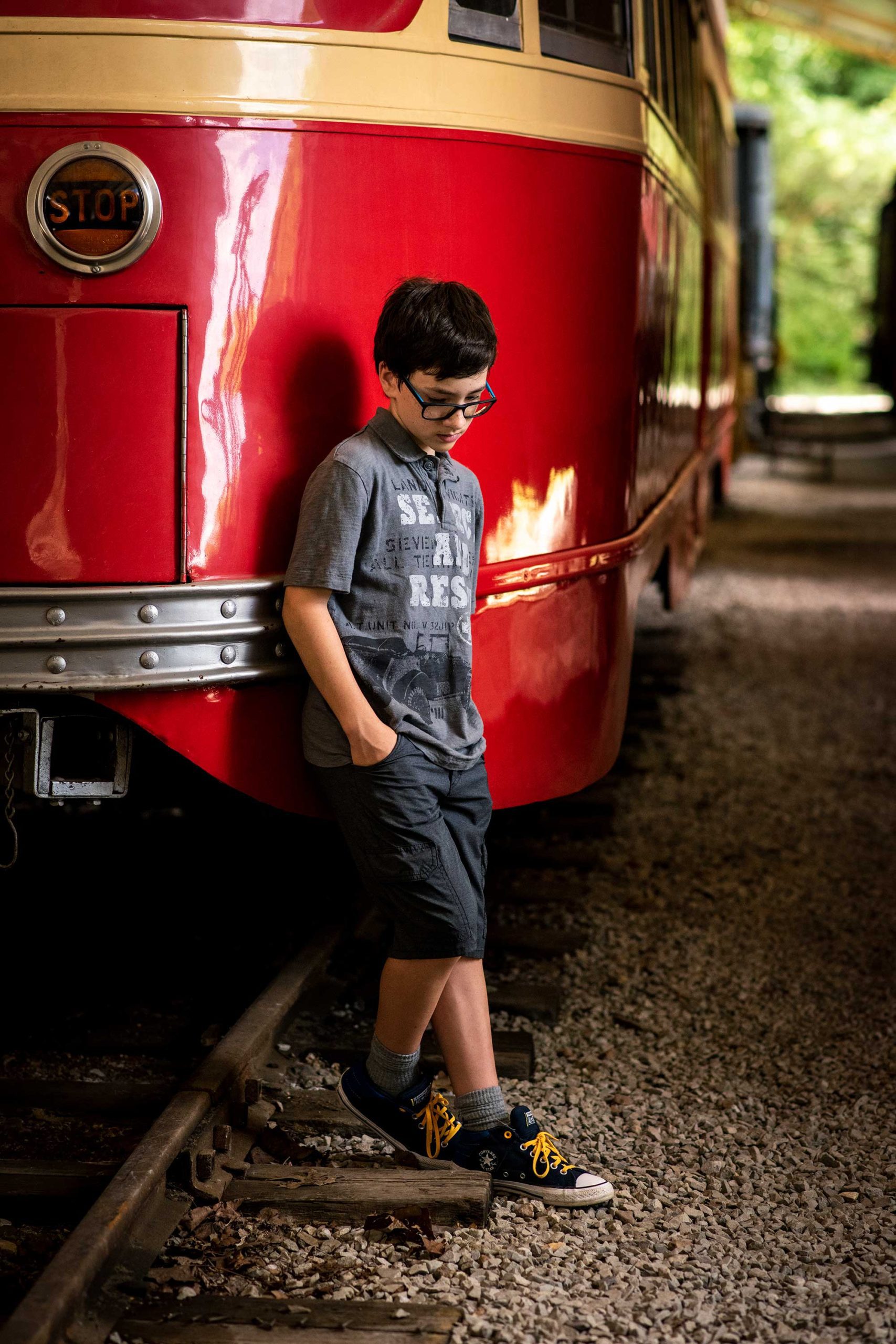 Young teen boy leaning against a red trolley car.