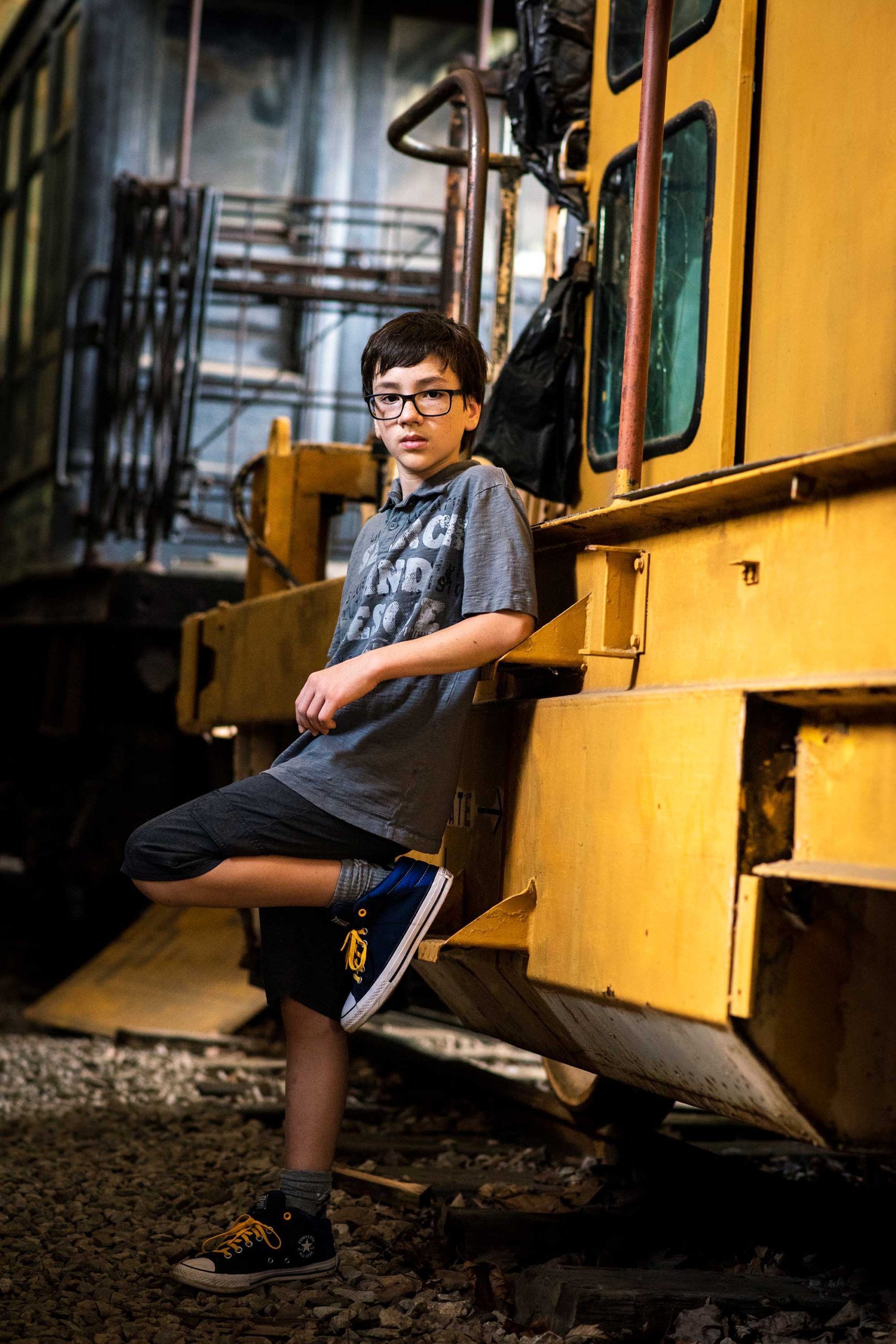 Young teen boy leaning against a yellow train.