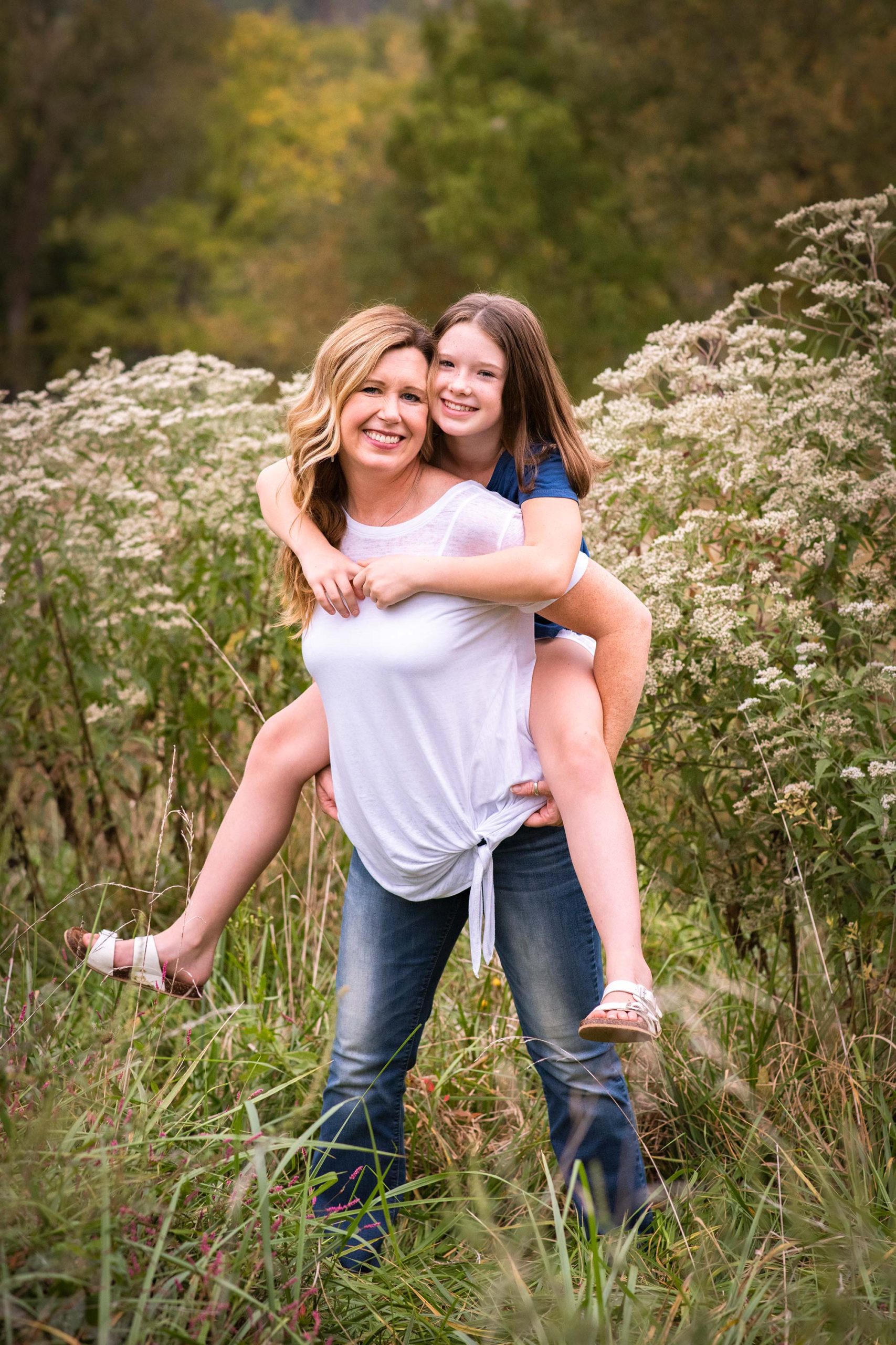 Tween daughter rides on mom's back in filed of flowers.