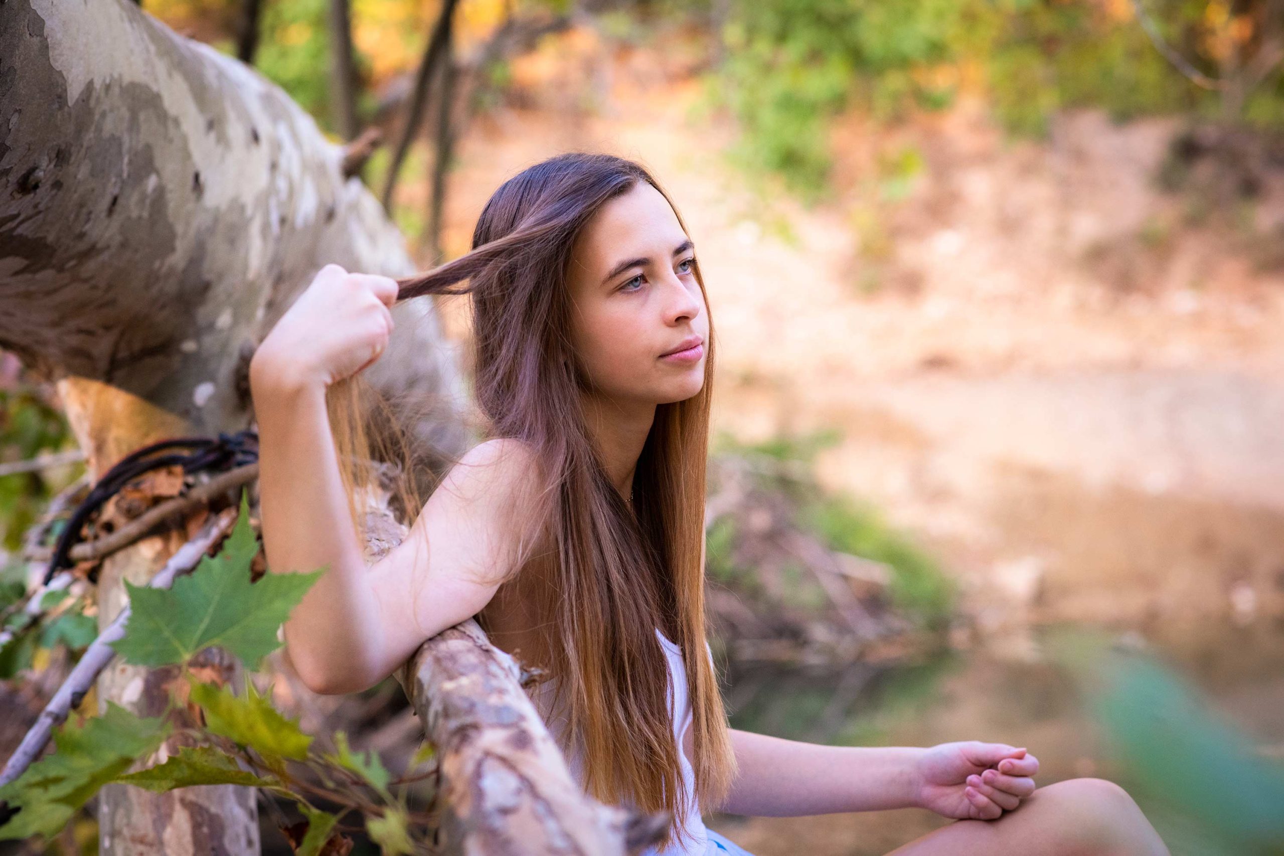 Senior girl leaning against a fallen tree in a creek bed.