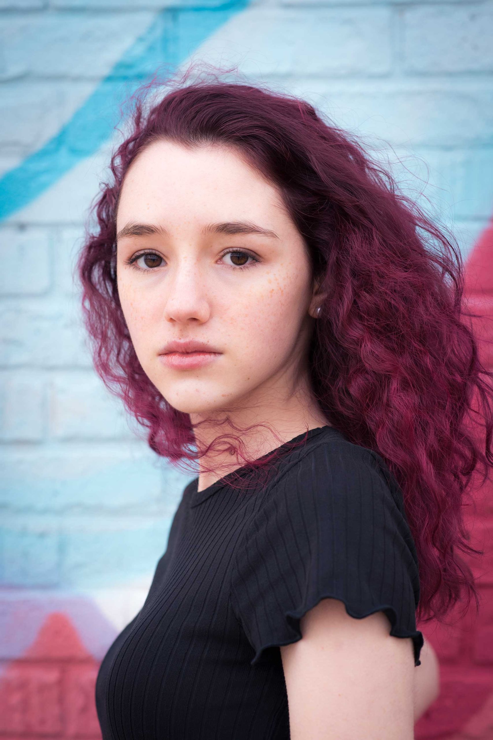 Teen girl with red colored hair against a graffiti wall.