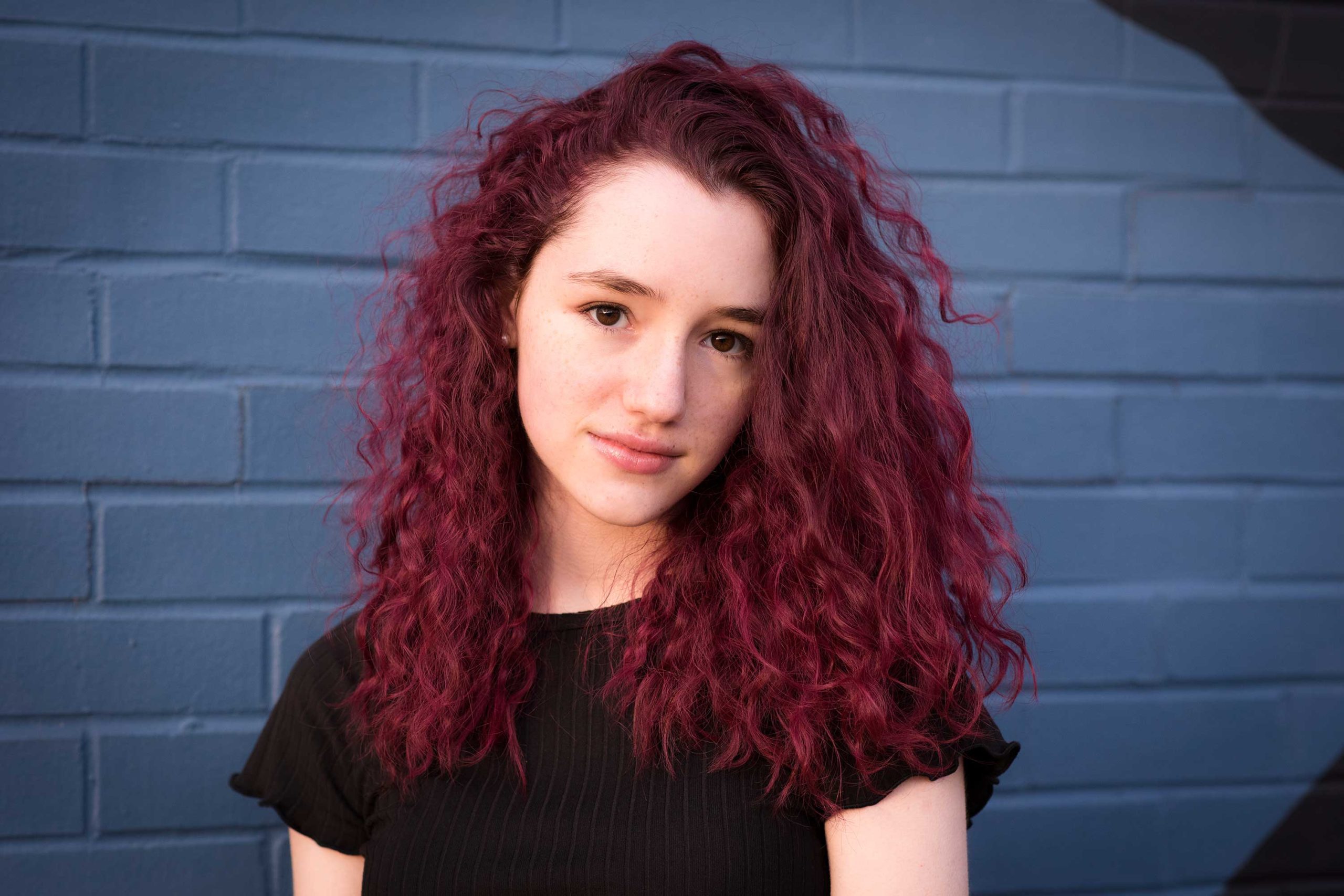 Teen girl with red colored hair against a blue graffiti wall.