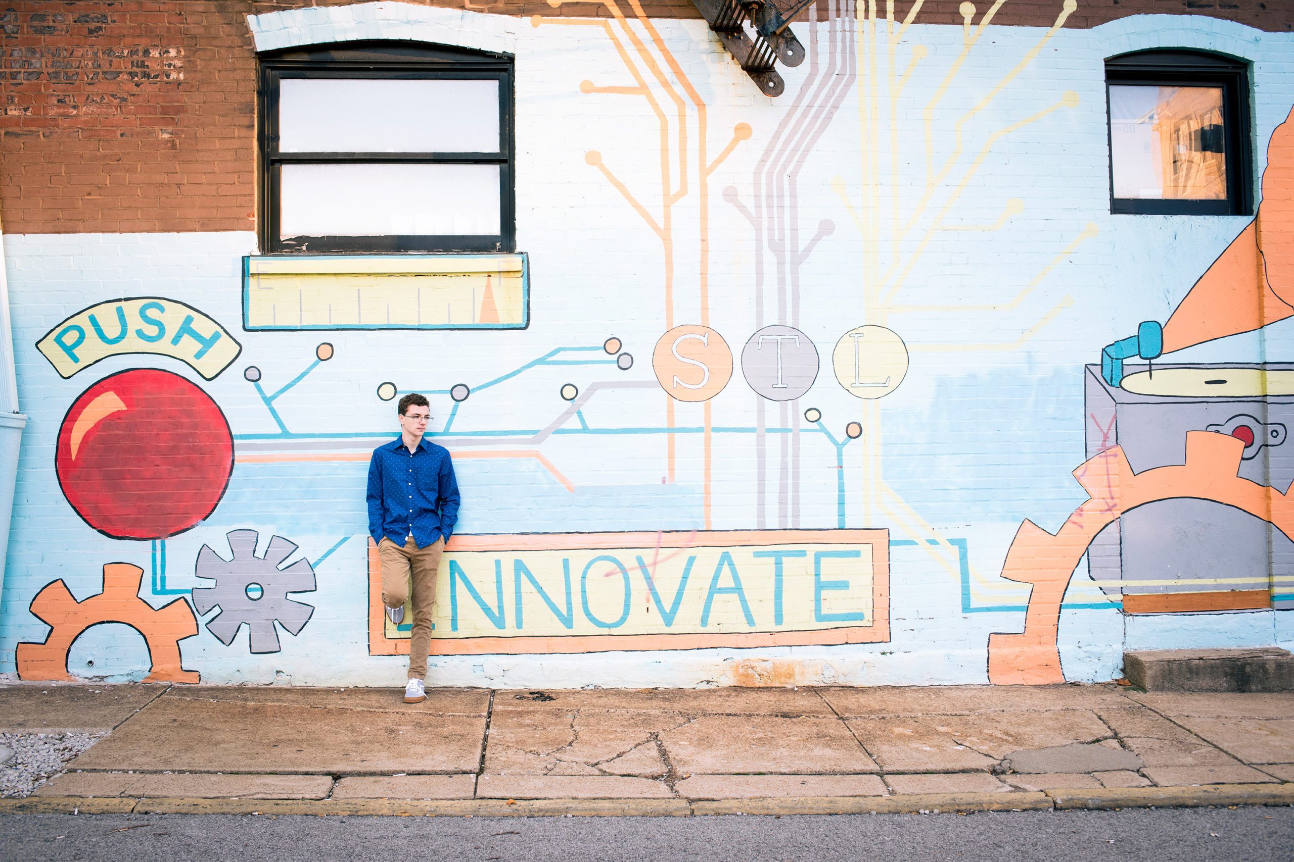 Senior Boy leaning against a wall mural that says "Innovate."