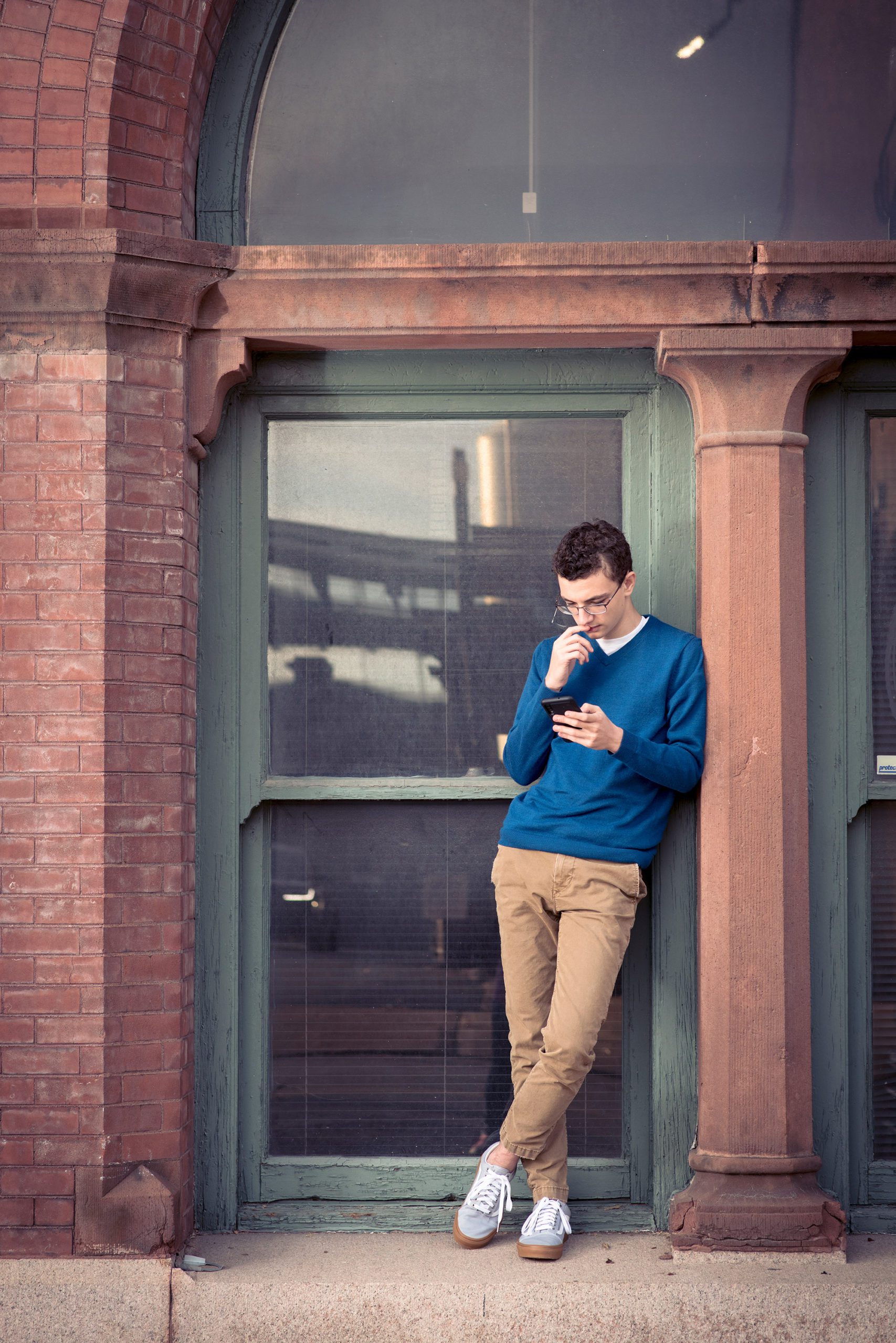 Senior Boy standing in window frame looking at phone.