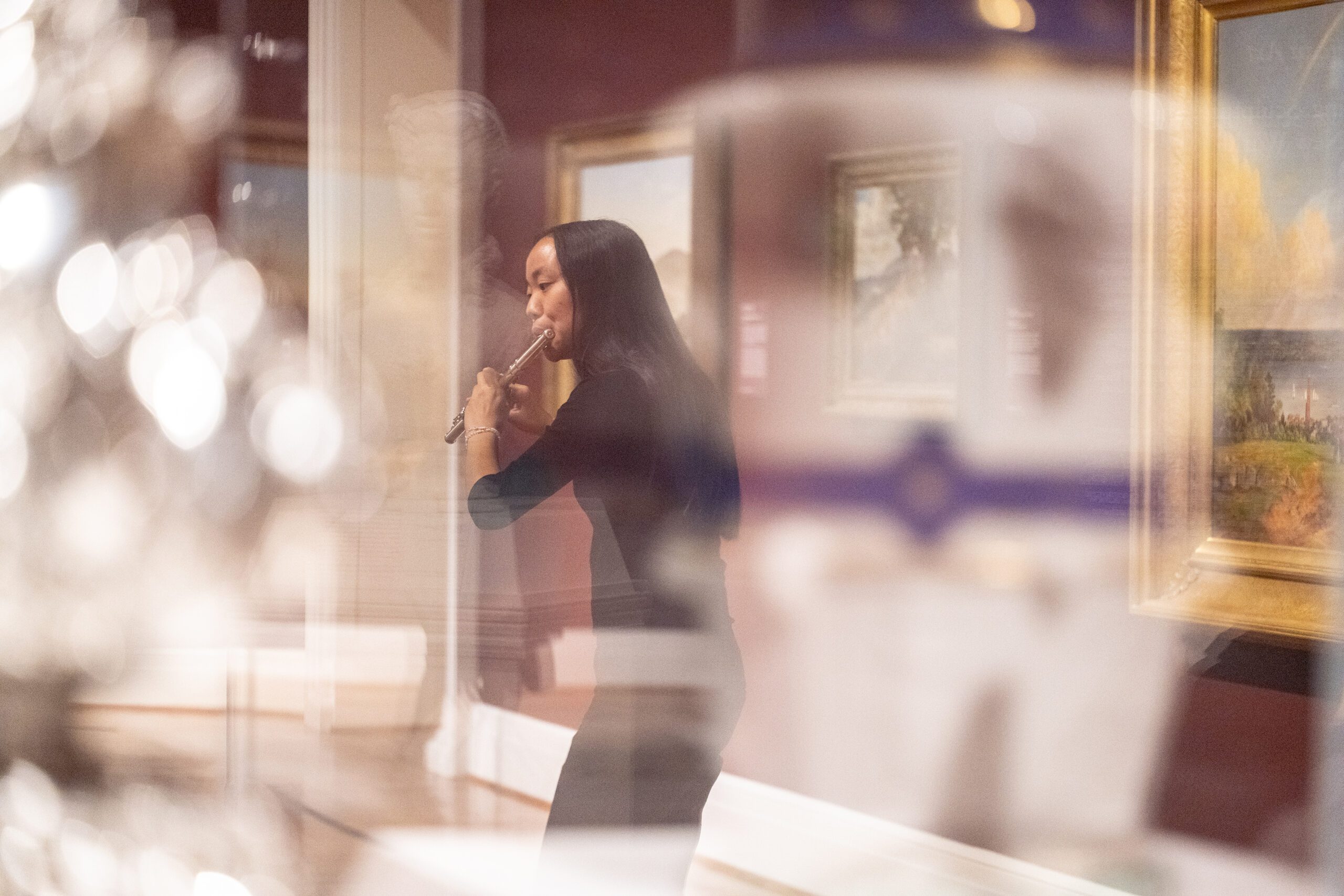 A WashU student plays the flute at the St. Louis Art Museum surrounded by paintings, sculptures and vases.