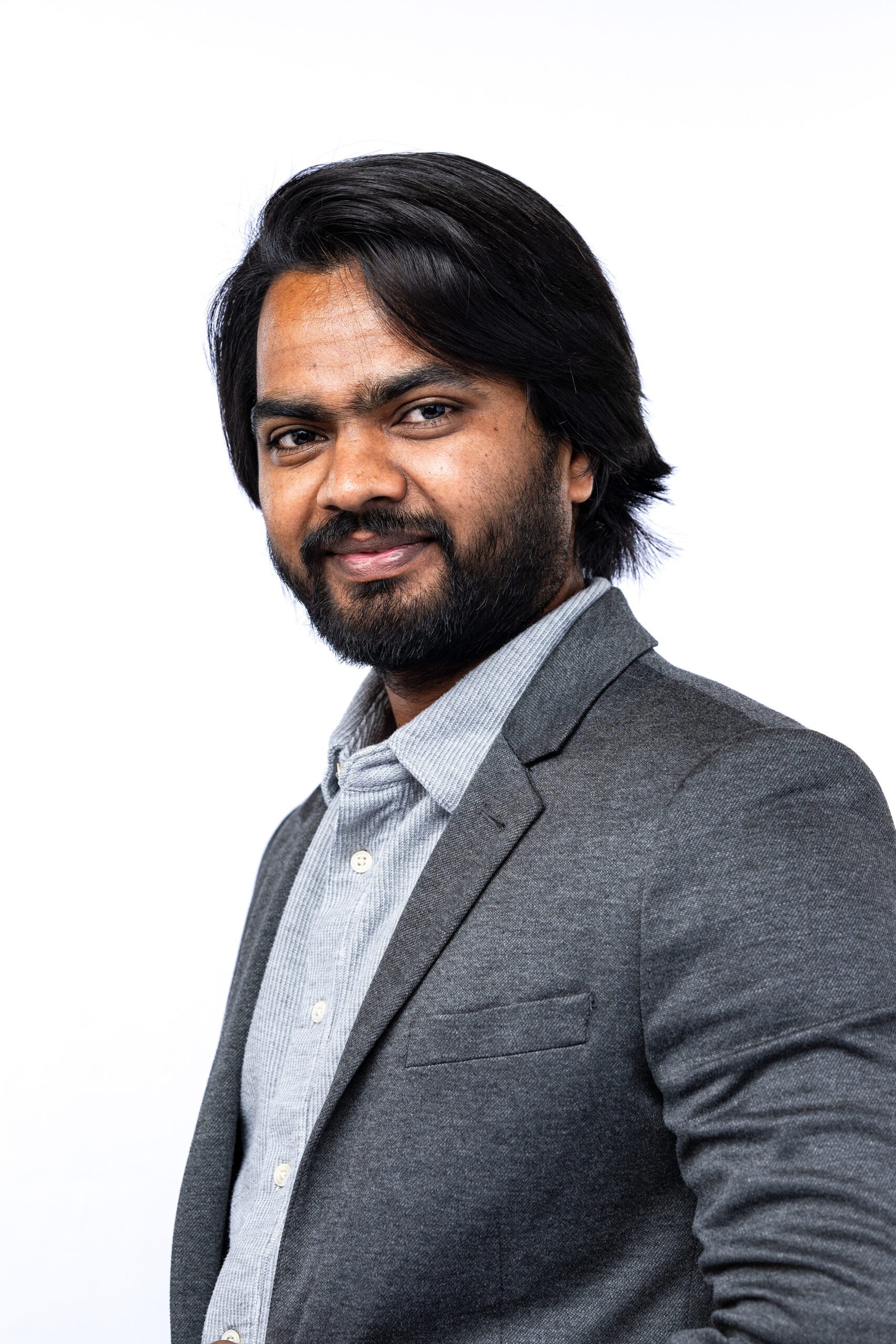 Headshot of a male in a grey jacket against a white backdrop.